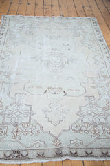 Distressed Oushak rug with faded ivory, seafoam green, and charcoal geometric pattern.