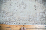 Lower section of a distressed Oushak rug, showing faded ivory and beige minimalist motifs.