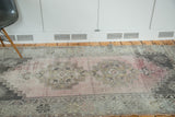 Angled view of distressed blush rose Oushak rug with geometric grey medallions.