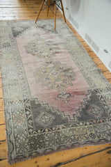 Fringed corner of a distressed geometric Oushak rug, displaying charcoal, ivory, and blush rose patterns.
