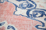 Distressed vintage Oushak carpet close-up, faded cherry red, blue scrolling arabesques.
