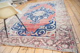 Distressed Oushak carpet corner with faded red field, bold blue scrolling motifs, and patterned border.