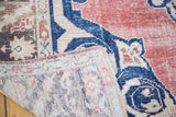 Distressed Turkish Oushak rug corner, faded cherry red pile, navy pattern, and hand-knotted back.