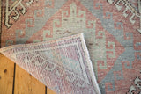 Distressed Oushak rug corner showing faded red, sea foam pile and hand-knotted back.