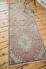 Distressed corner of Oushak runner with faded cinnabar red and soft sea foam rectilinear design.