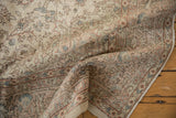Curled distressed Oushak rug showing intricate floral motifs in faded blush rose, powder blue, and celadon.