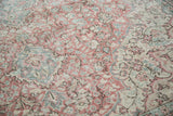 Softened blush rose, celadon green, and ivory floral patterns on this distressed Oushak rug.