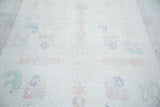 Distressed Oushak carpet texture, faded ivory field with subtle pastel motifs.