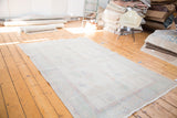 Softly faded distressed Oushak rug with muted pastel patterns on an ivory field.