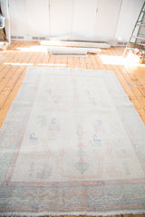 Distressed Oushak carpet, faded ivory field with minimalist pastel patterns.