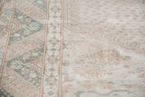 Distressed Oushak carpet with faded hook motifs in soft green and beige.