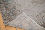Folded corner of distressed Oushak carpet, revealing hand-knotted texture and muted silver, grey, green tones.