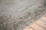 Distressed Oushak carpet corner with soft green running hook border and faded pattern.