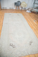 Distressed Oushak runner showing exposed foundation and faded apricot peach spandrel.