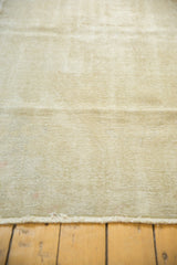 Distressed Oushak rug with worn muted beige and ivory pile texture and fringe.