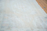 Distressed Oushak rug with low pile showing faded ivory, beige, and rose patterns.