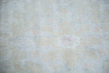 Distressed texture of the Oushak rug, showing muted ivory, beige, and pink rose tones.
