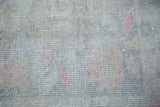 Distressed Oushak rug pile, showing faded intricate detail in beige, ivory, and pink rose.