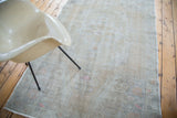 Faded texture of a distressed Oushak rug with ivory, beige, and rose pink hues.