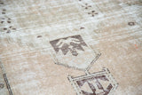 Distressed Oushak runner's faded tribal geometric medallion with apricot peach and moss green.