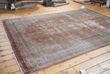 Distressed Oushak rug texture with faded brown field and subtle red border pattern.