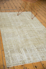 Distressed Oushak rug corner showing faded ivory, soft sage, and charcoal geometric patterns.
