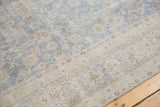 Distressed Oushak rug detail, featuring worn pile with muted blue and beige floral palmettes.
