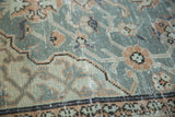 Distressed slate blue and blush rose Oushak rug with scrolling vine motifs.