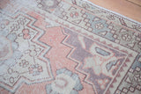 Distressed Oushak runner's faded brick red field and geometric beige, celadon, charcoal motifs.