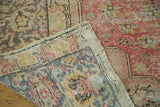Distressed hand-knotted Oushak rug corner, showing backing, fringe, and worn red and blue patterns.