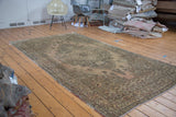 Distressed Oushak carpet, angled view, ornate medallion in dusty beige, bronze, and grey.