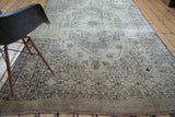 Distressed texture and geometric border patterns in charcoal and beige on Oushak rug.