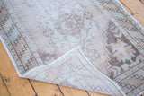 Distressed Oushak rug pile showing faded ivory, beige, and brown motifs, with visible hand-knotted backing.