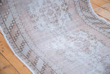 Faded geometric border and worn pile texture of a distressed Oushak runner in beige and rose.