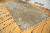Distressed Oushak rug corner displaying faded geometric border, neutral tones, and fringed edge.