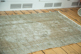 Distressed Oushak rug corner, revealing textured, receded pile and foundation with fringe.