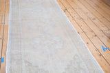 Distressed Oushak runner's side, with faded curvilinear ivory and beige patterns.