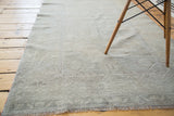 Distressed Oushak rug surface with faded beige rectilinear patterns and short fringe.