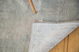 Distressed beige and silver Oushak rug pile revealing hand-knotted foundation and fringe.