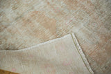 Folded corner of distressed dusty rose Oushak rug, revealing its hand-knotted backing.
