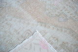Distressed pile texture with muted ivory and beige tones, showing hand-knotted rug foundation.