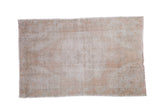 Distressed Oushak rug with worn texture, muted ivory, beige, and rose tones.