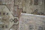 Distressed Oushak rug showing geometric patterns, textured pile, and visible woven foundation.