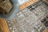 Geometric motifs, wide border, and distressed exposed foundation in muted brown and black.