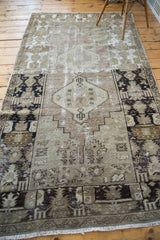 Textured, distressed Oushak rug corner with geometric patterns in soft grey, sage, black.