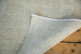 Distressed light-toned Oushak rug corner revealing soft pile, fringe, and hand-knotted foundation.