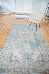 Distressed Oushak rug corner featuring teal, ivory, charcoal, prawn border, and trefoil spandrel.