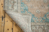 Distressed Oushak rug corner showing hand-knotted back, faded peach, and aqua green pile.