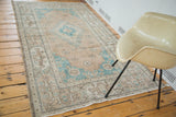 Distressed Turkish Oushak rug corner with soft aqua spandrel, peach field, and muted border.