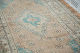 Vintage Oushak rug's distressed texture, with faded peach and aqua green motifs.